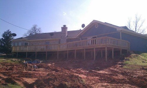 A large house with a large wooden deck sitting on top of a dirt hill.