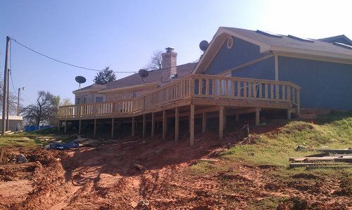 A house with a large wooden deck sitting on top of a dirt hill.
