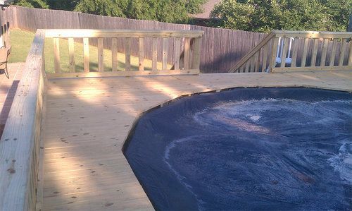 A wooden deck overlooking a swimming pool with a fence in the background