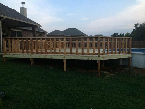 A wooden deck is sitting next to a pool in a backyard.