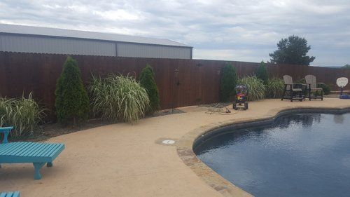 A wooden fence surrounds a swimming pool in a backyard.