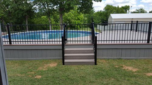 A fence surrounds a swimming pool with stairs leading to it.