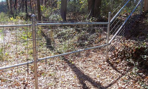A metal fence is surrounding a dirt path in the woods.