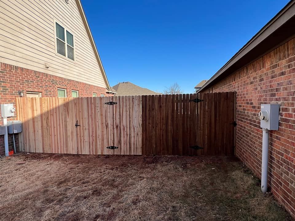 A wooden fence is in the backyard of a brick house.