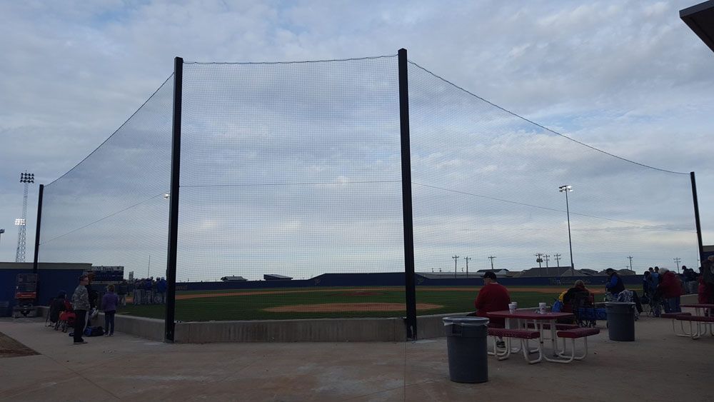 A group of people are sitting at picnic tables in front of a baseball field