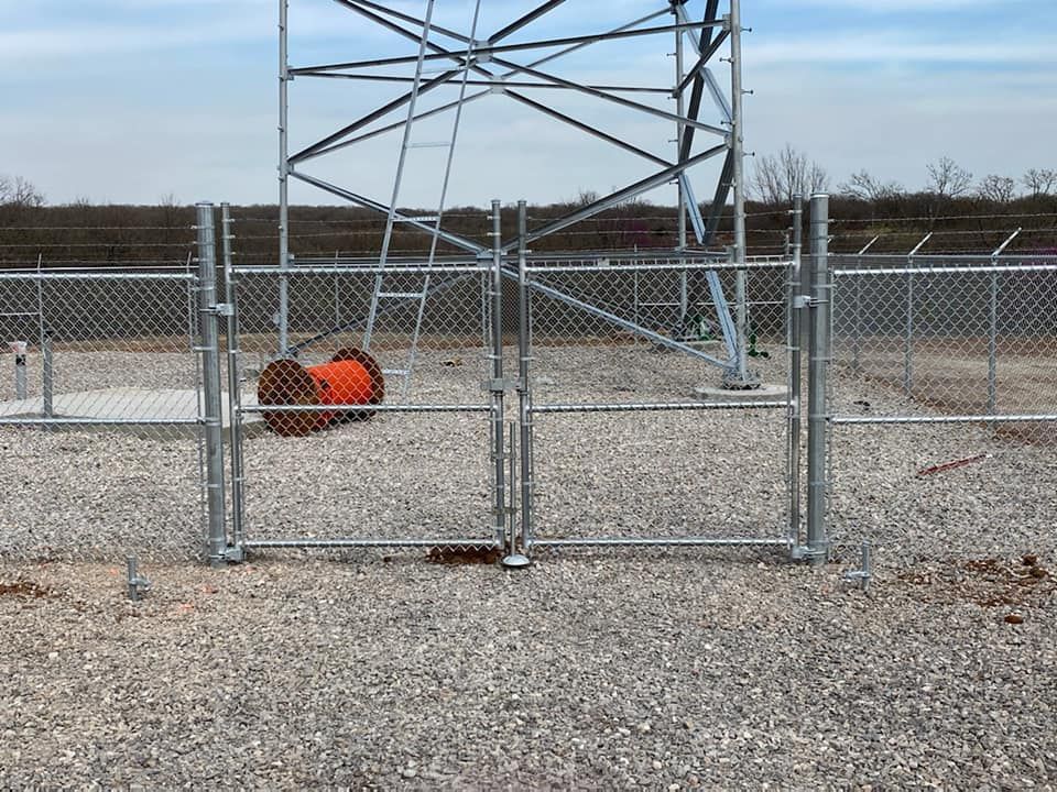 A chain link fence surrounds a gravel area with a tower in the background