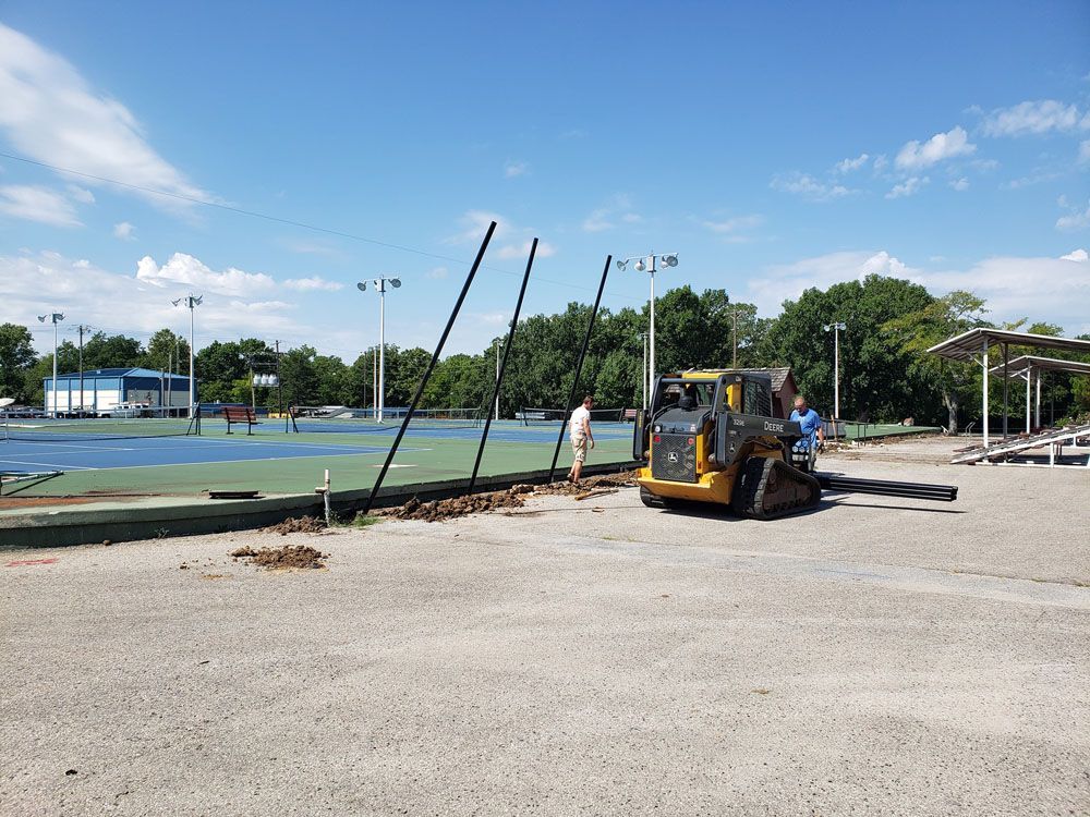 A bulldozer is sitting in a parking lot next to a tennis court