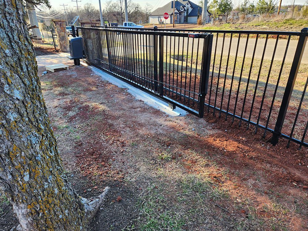 A black fence with a tree in the foreground and a sliding gate in the background