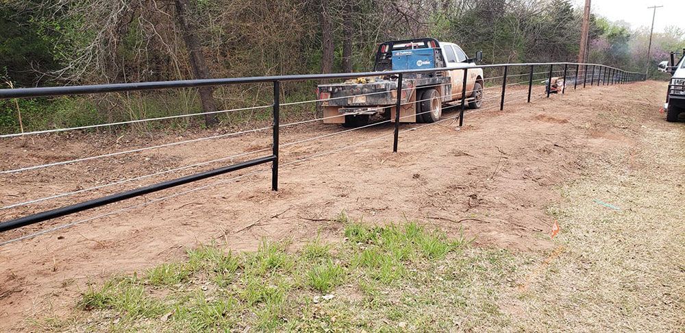 A truck is parked on the side of a dirt road next to a fence