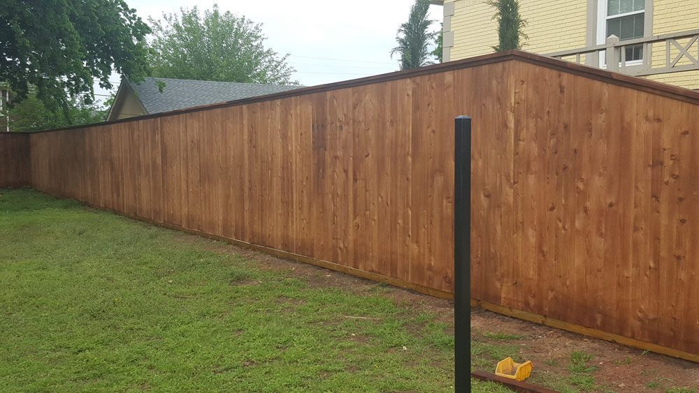 A wooden fence surrounds a lush green yard in front of a house