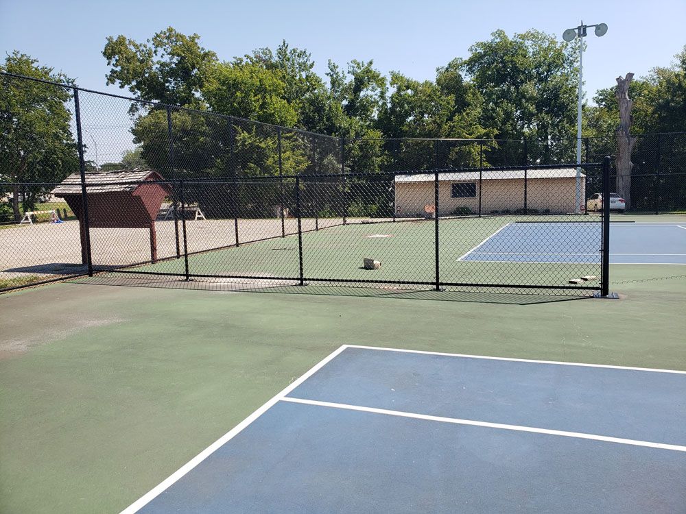 A tennis court with a fence around it and trees in the background