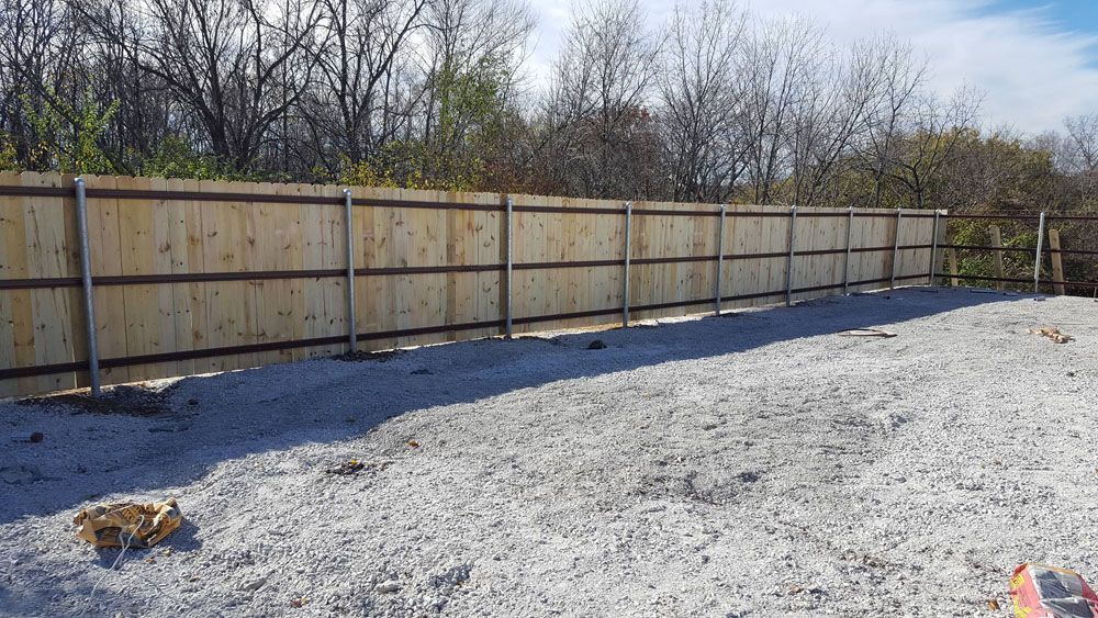 A wooden fence surrounds a gravel area with trees