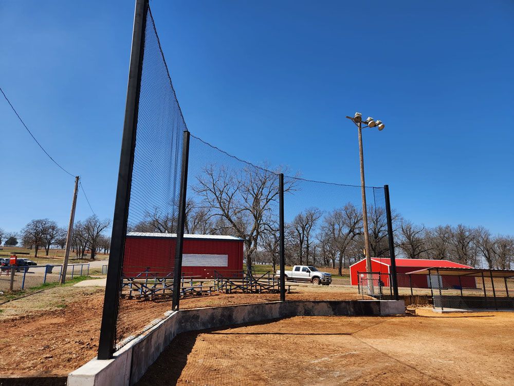 A baseball field with a fence and a red barn in the background