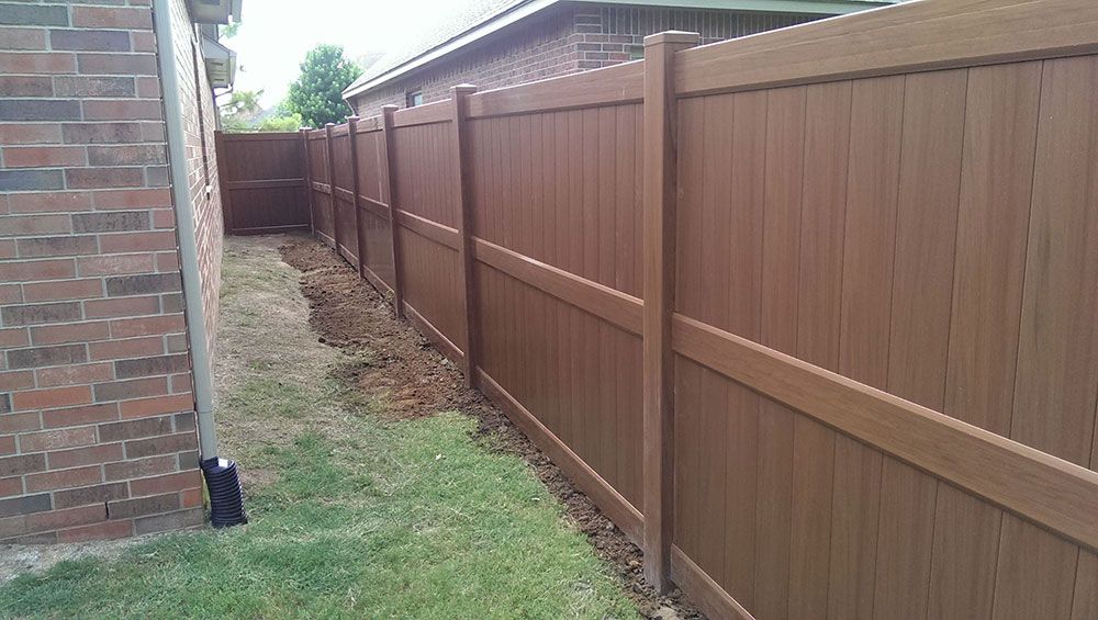 A wooden fence surrounds a brick house in a backyard