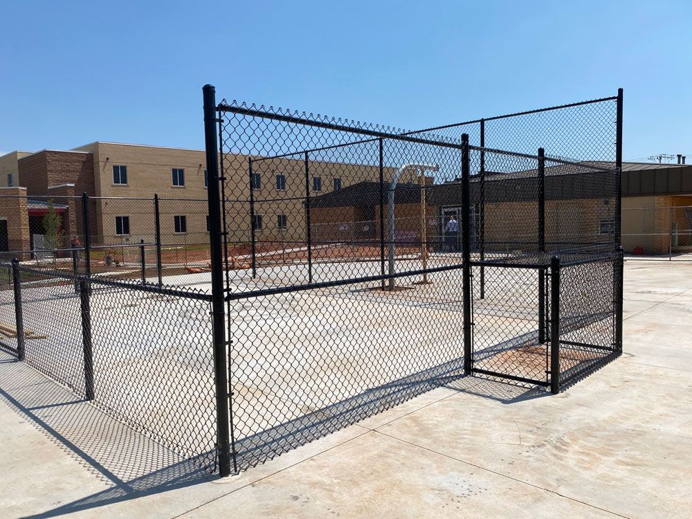 A chain link fence surrounds a basketball court in front of a building