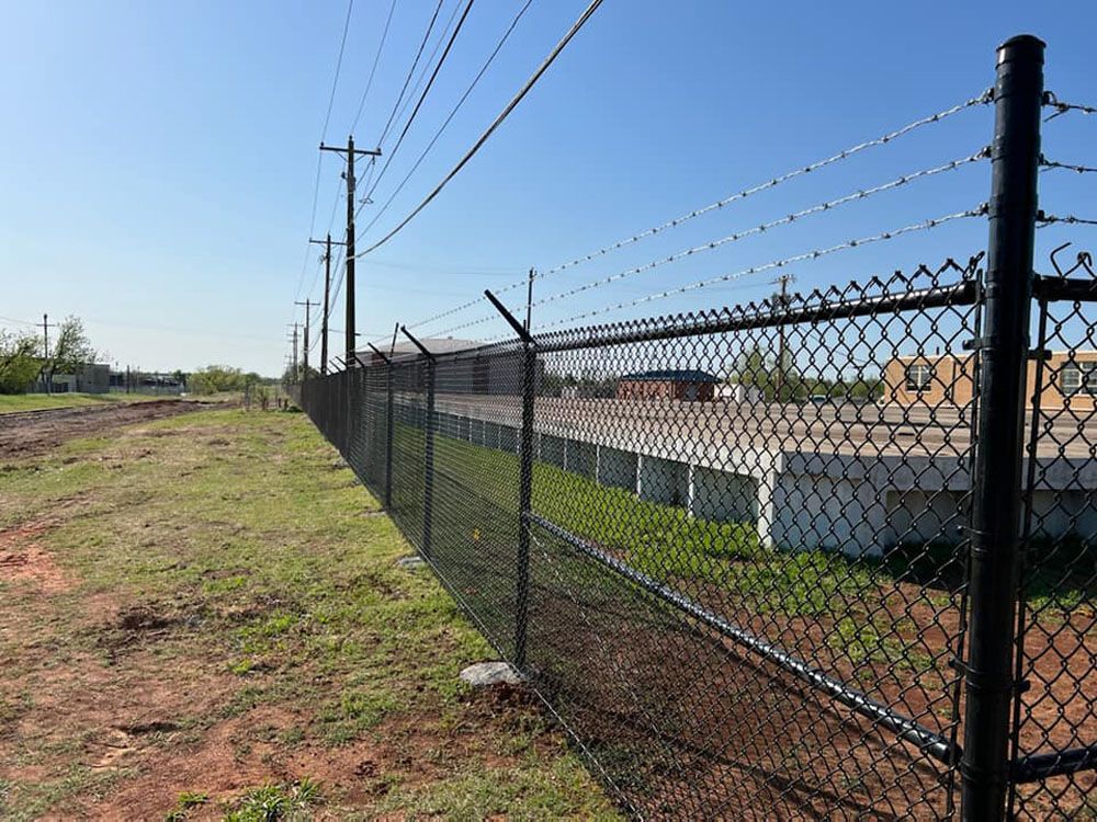 A chain link fence with barbed wire along the side of a field