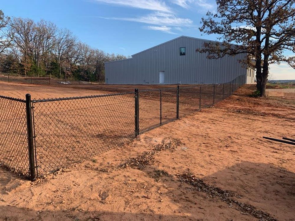 A chain link fence surrounds a large building in a dirt field