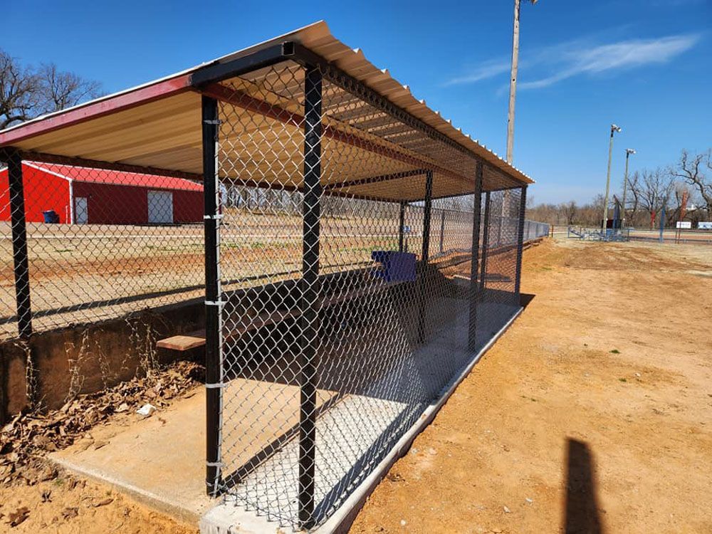 A chain link fence shelter with a red barn in the background