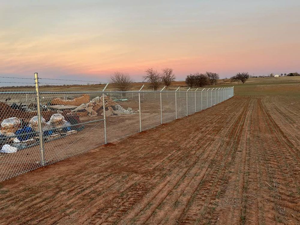 A chain link fence surrounds a dirt field at sunset