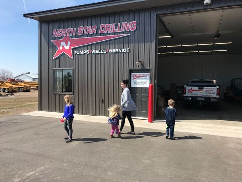 Yellow drilling machine working on construction site, near a truck, with trees in the background.