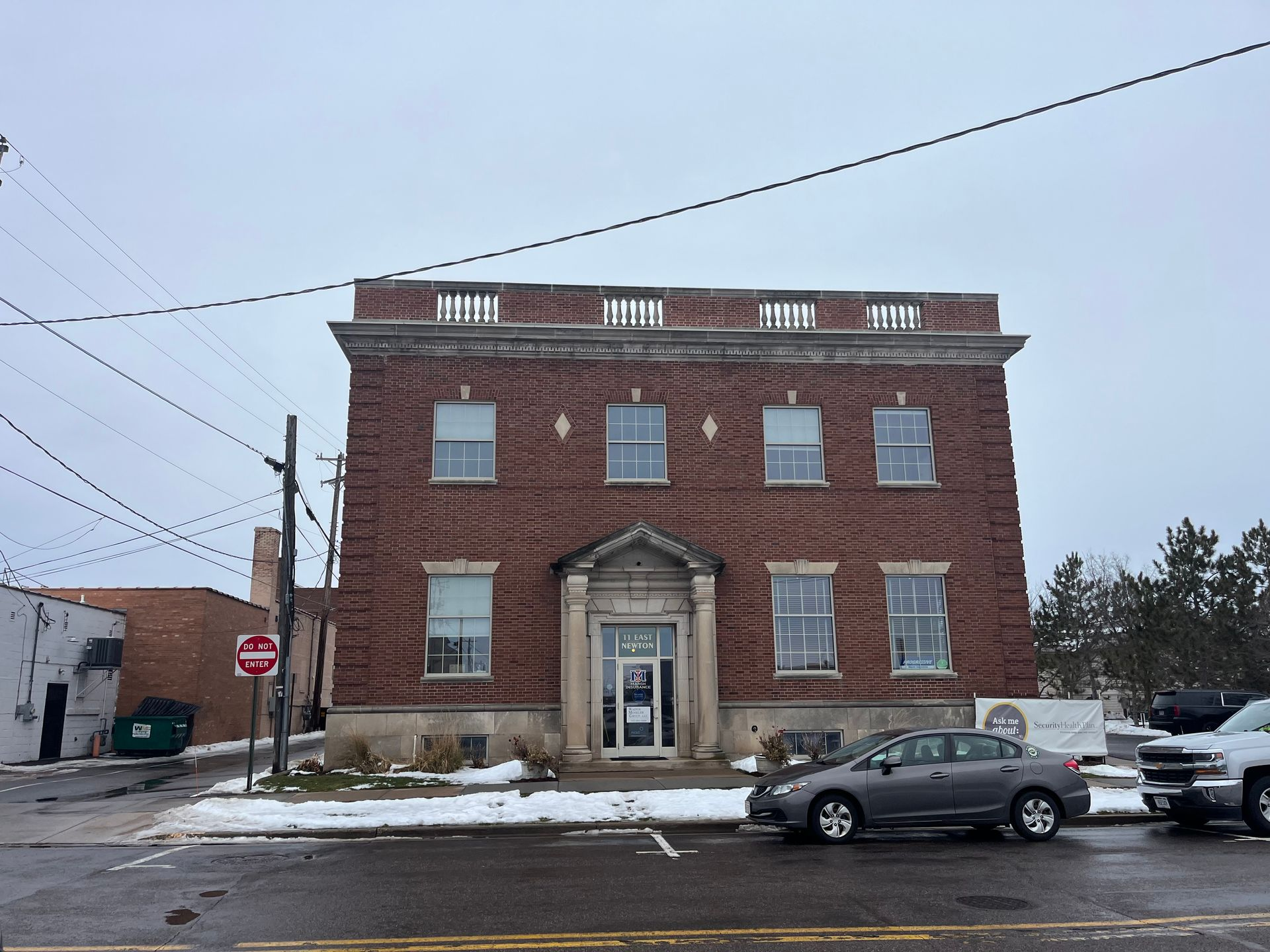 Beige, multi-story building with columns, windows, and a small entrance under a porch.