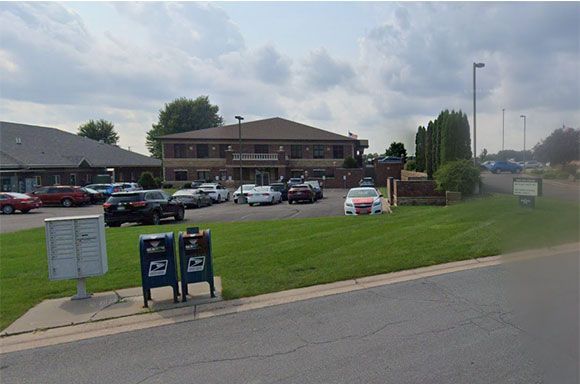 Postal mailboxes in front of a building with a parking lot; cars parked, green grass, and blue sky.