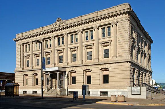 Beige, multi-story building with columns, windows, and a small entrance under a porch.