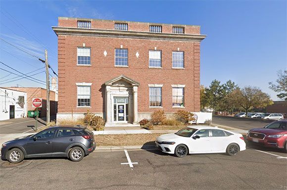 Brick building with cars parked in front, sunny day.