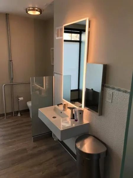 Modern bathroom with floating sink, illuminated mirror, and stainless steel trash can.