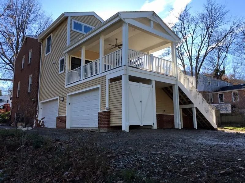 Two-story house with a balcony and garage; tan siding, white trim, and a brick facade.