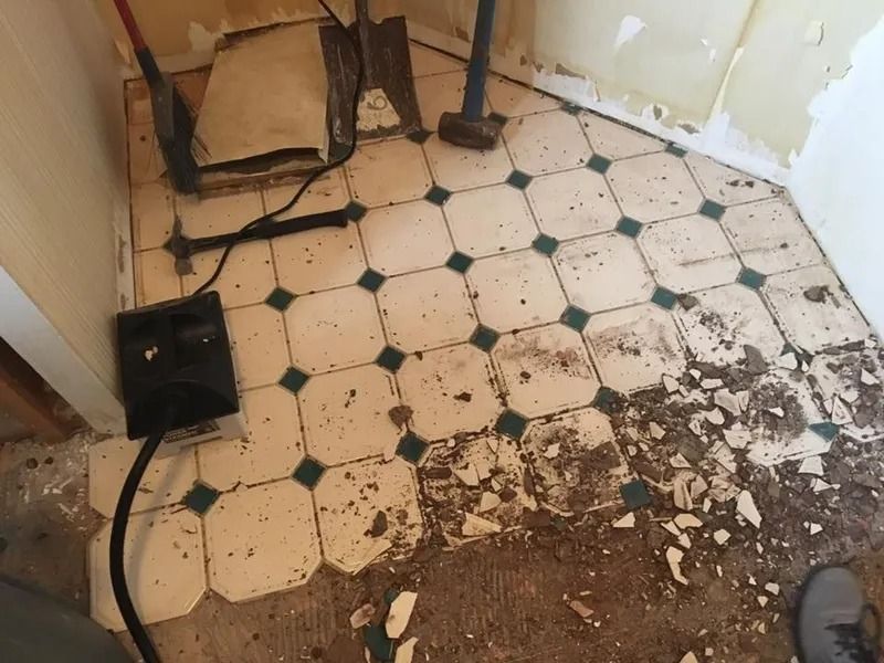 Bathroom floor being demolished, white and teal tile with debris and tools.