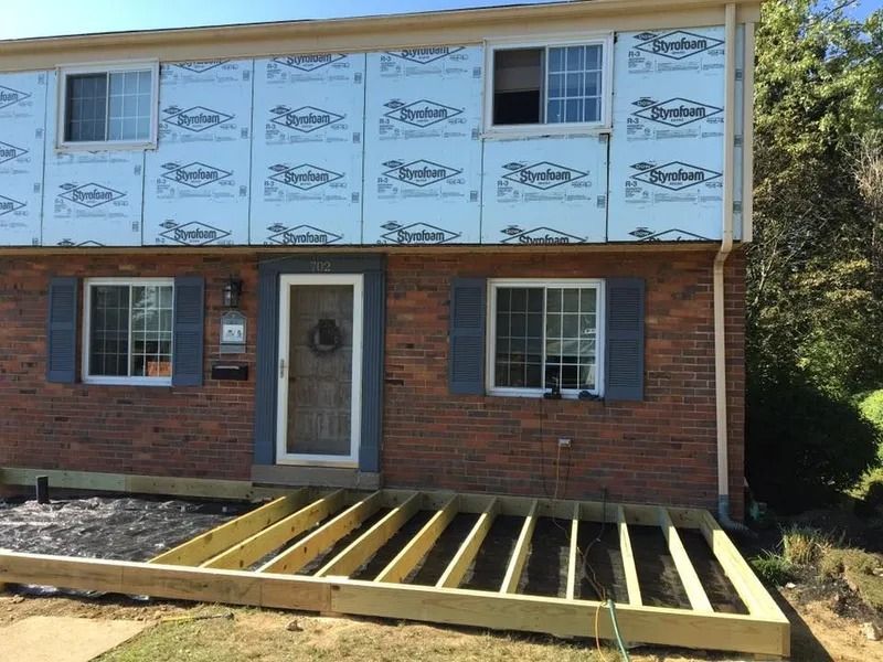Exterior of a two-story brick building under construction with a deck frame and exposed sheathing.