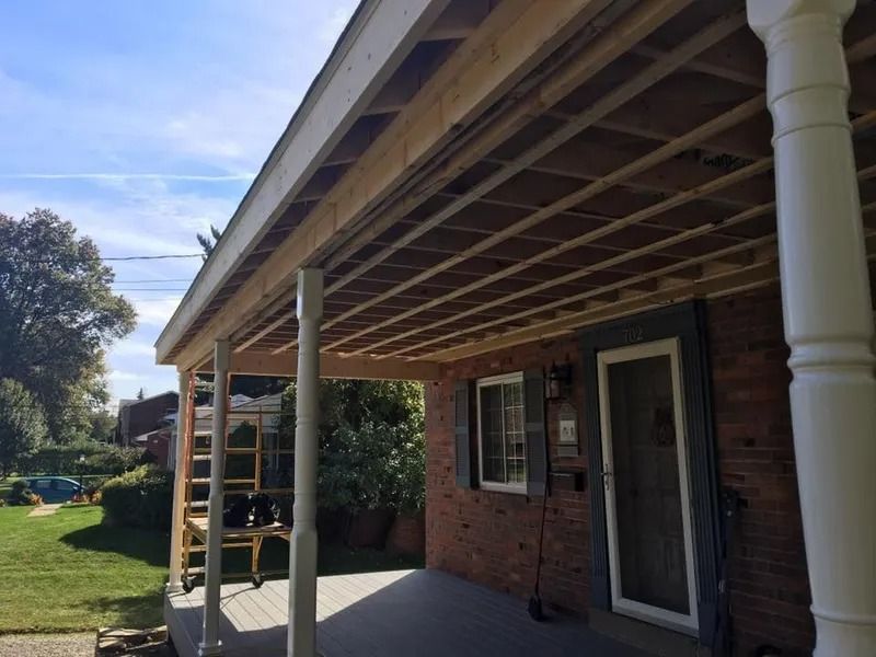 Porch roof under construction, visible beams, columns, and a brick house.