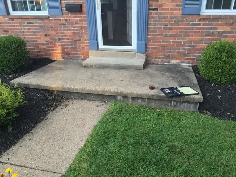 Concrete porch with path, door, brick house, and green lawn.