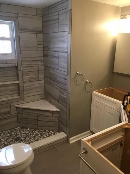Bathroom with tiled shower stall, corner seat, and pebble floor, toilet, and vanity under construction.