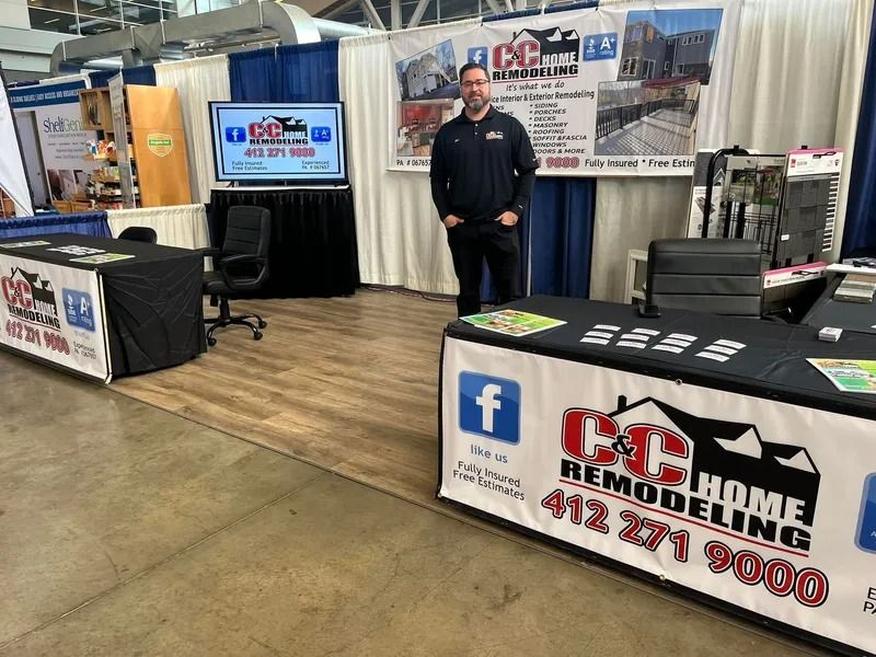 Man at CC Home Remodeling booth at a trade show. White banner and logo on display tables. Blue and white backdrop.