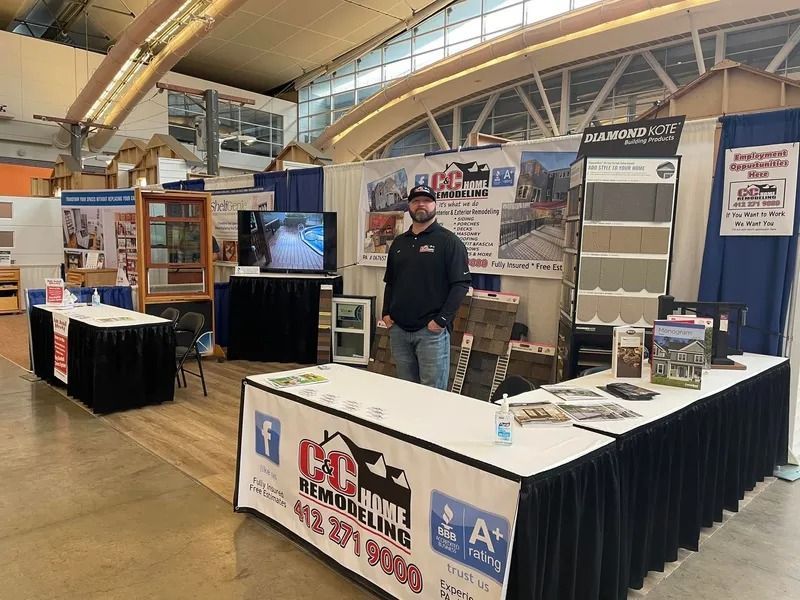 Man stands at a home remodeling booth at a trade show. Booth has signs, samples, and a TV.