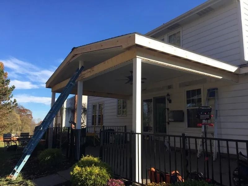 House with a covered patio under construction, ladder leaning against it. Sunny day, blue sky.