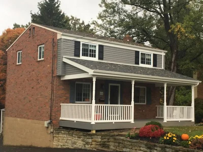 Two-story house with brick and gray siding. A porch with white railings and a gray deck.