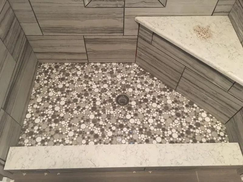 Shower with gray and white tile, a mosaic floor, and a white corner seat.