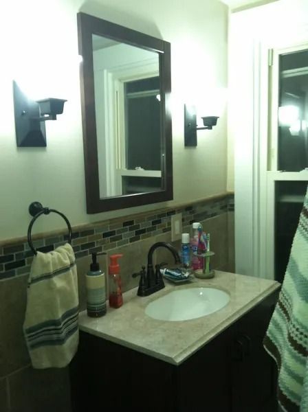 Bathroom with dark brown vanity, mirror, and sconces; sink with toiletries, and towel racks.