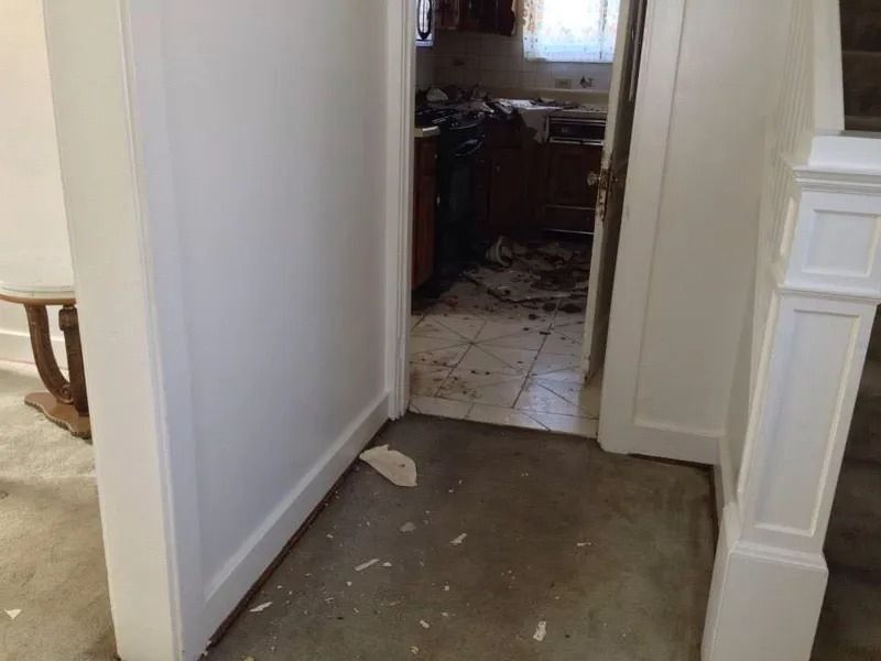 Entryway with door frame leading to a kitchen with debris on the floor and in the background.