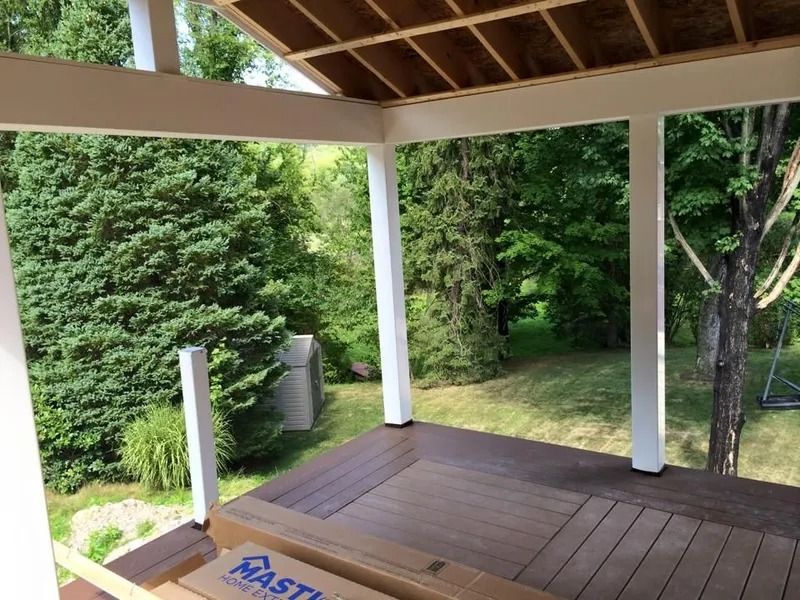 A partially built deck with white pillars, brown decking, and a view of green trees.