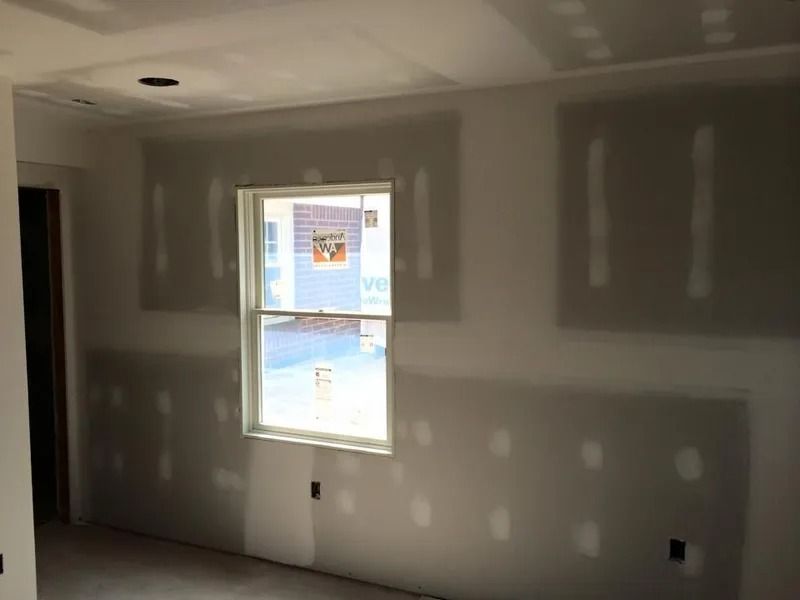 Room under construction with drywall installed around window and electrical outlets.