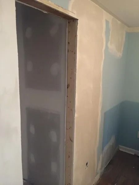 Interior view of a room with a doorway and walls covered in drywall and joint compound. Blue paint is visible.