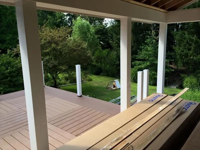 Covered deck with white columns, composite decking, and boxes, overlooking a green yard and trees.