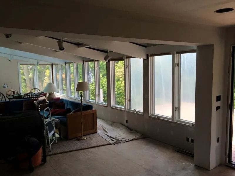 Interior room under construction with large windows and a partial view of trees.