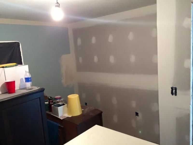 Room interior during renovation; blue and gray painted walls, drywall patched, desk with items.