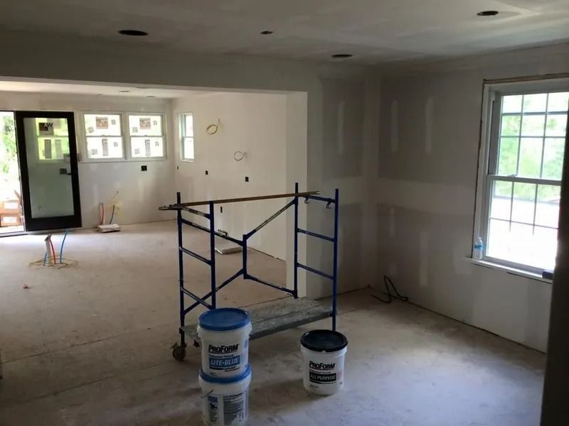 Interior of a room under construction with drywall and scaffolding, featuring windows and an open doorway.