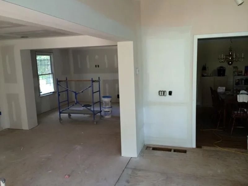 Interior of a house under construction; drywall and exposed studs visible, scaffolding, and open doorway.